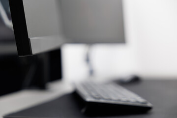 dettagli di una postazione da lavoro in un ufficio con pareti bianche e un tavolo nero con tastiera e schermo per computer fisso