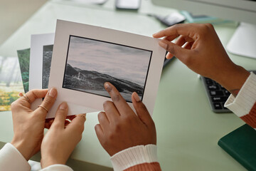 Close up of two women holding photo prints with nature landscapes and discussing images for creative project copy space