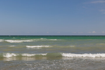 dettagli di un ambiente di mare, in estate, di giorno, con cielo sereno, visto dalla riva, guardando verso l'orizzonte, mentre le onde basse raggiungono la costa