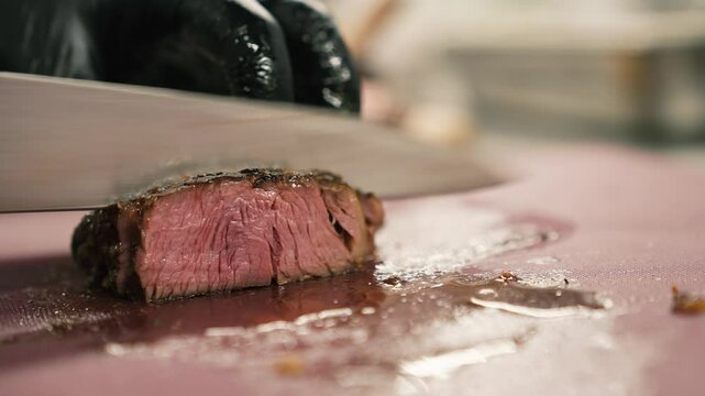 Chef in black gloves slices a freshly cooked beef steak with a knife. Cook cuts a hot piece of meat on a kitchen board. Close-up. 4k footage