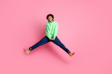 Full body portrait of cool young man jump empty space wear green hoodie isolated on pink color background