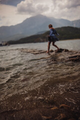 Fototapeta premium A person walks barefoot on rocky shoreline during golden hour against a backdrop of mountains