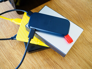 Pile of different sized external storage hard drives, wooden background