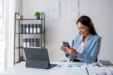 A woman is sitting at a desk with a laptop and a cell phone