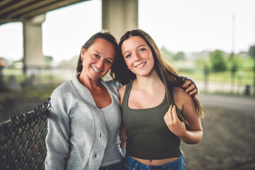 Relationship parent and teenager, hugging smiling mother and daughter, urban background