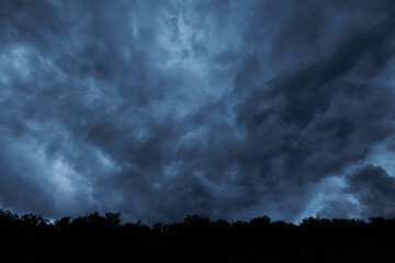 cielo molto nuvoloso, con nuvole cariche di pioggia e minacciose, dalle sfumature di colore azzurro, di sera, prima di un temporale, viste da sotto un bosco in collina