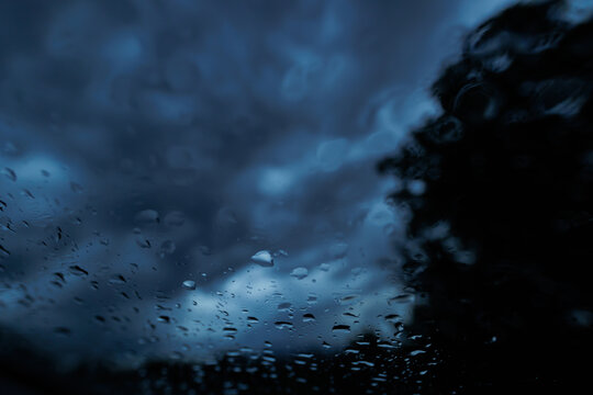 gocce di pioggia sul vetro trasparente di un'automobile in primo piano, cielo minaccioso, scuro e coperto da nuvole blu, di sera, sfuocato sullo sfondo