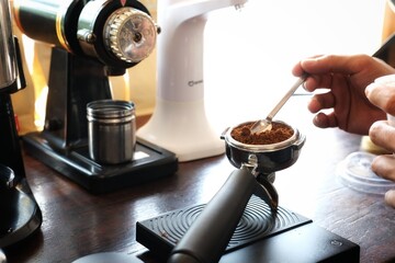 Close-up of a barista's hand precisely leveling ground coffee in a portafilter. Perfect for coffee-related content, barista tutorials, or showcasing professional coffee preparation techniques.