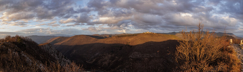 ampia composizione panoramica con vista su varie catene di montagne e alture nella Slovenia occidentale, vicino al confine Italiano, di pomeriggio, in inverno, al tramonto, sotto un cielo nuvoloso