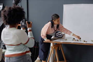 Portrait of Black young woman with braided hair as photographers assistant setting up for product photoshoot in studio copy space