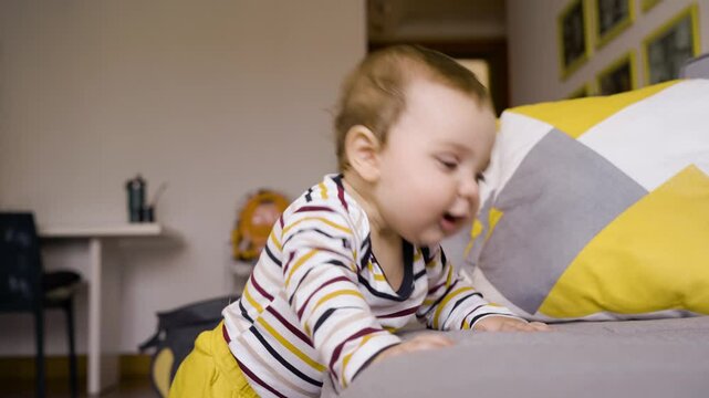 Smiling Baby Learning to Walk, Holding Onto Couch. Adorable Infant in Striped Onesie Standing with Support, Drooling Happily in Living Room