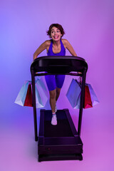 Photo of joyful sporty girl running fast on treadmill shopaholic buying on sport sales isolated ultraviolet color background