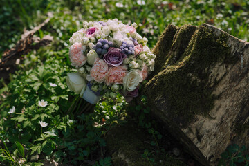 A bouquet of flowers is placed on top of a mossy log. The flowers are a mix of pink and purple, and...