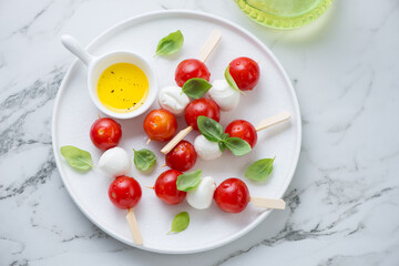 White plate with italian caprese skewers and olive oil, horizontal shot on a white marble surface, high angle view