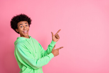 Portrait of nice young man indicate fingers empty space wear green hoodie isolared on pink color background