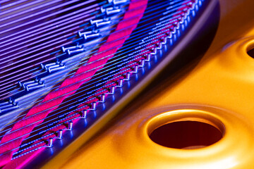 View of the inner workings of a classical concert grand piano with sides of different lengths, which are made to sound by striking them. Colorfully illuminated details of handcrafte musical instrument