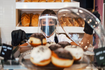 Beautiful young female worker with protective mask  and face shield working in bakery. Business and coronavirus pandemic concept.