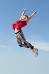 cheerful little girl jumping high in blue sky
