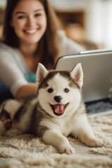 Fototapeta premium Smiling woman and husky puppy with a laptop indoors.