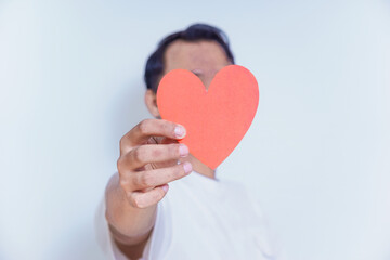 A person holds up a red heart-shaped cutout, symbolizing love and affection against a clean white background. World Heart Day concept