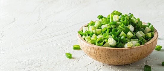 A wooden bowl holds chopped spring onions on a white table providing ample copy space in the image