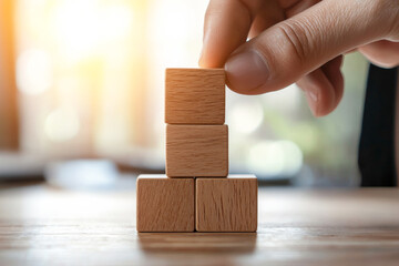A hand arranging wooden blocks in a stack, symbolizing creativity, growth, and construction in a bright environment.