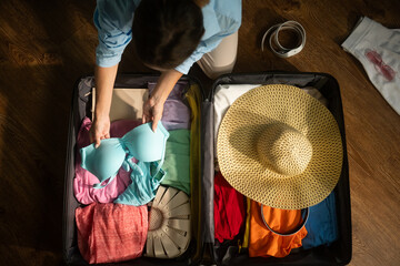 Woman organizes clothing items in an open suitcase, preparing for a vacation or business trip. Careful packing ensures essentials are ready for travel adventures