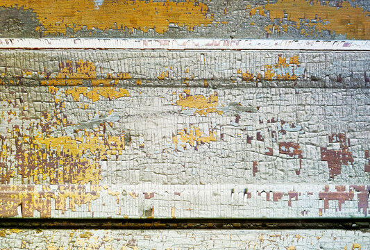 Full frame background texture of weathered horizontal wooden paneling with flaking white and yellow paint layers, showing fine micro cracks and heavily distressed grunge patterns.