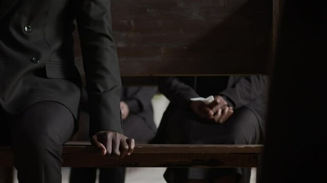 Three unrecognisable people sitting on wooden benches during funeral ceremony in church