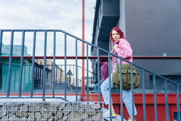 Portrait of young woman with bright haired wearing pink jacket smiling, immersed in the urban scenery.