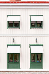 Grüne Fenster vor weißer Holzfassade. Skandinavische Architektur. Green windows in front of a white wooden façade. Scandinavian architecture.