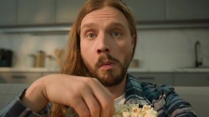 Portrait concentrated focused funny Caucasian bearded man guy male at home couch sofa relaxing watching TV television series move film program sport championship football game eating popcorn obesity