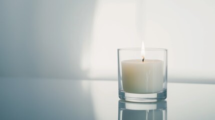 Simple white candle burning in a glass jar, set on a reflective surface with a window shadow in the background, creates a serene and peaceful atmosphere