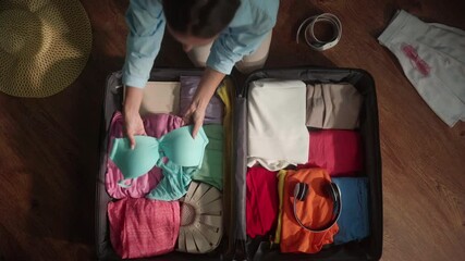 Woman organizes clothing items in an open suitcase, preparing for a vacation or business trip. Careful packing ensures essentials are ready for travel adventures
