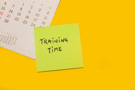 Concepto de tiempo de entrenamiento escrito en un post it junto a un calendario sobre un fondo amarillo. Vista superior y de cerca. Copy space