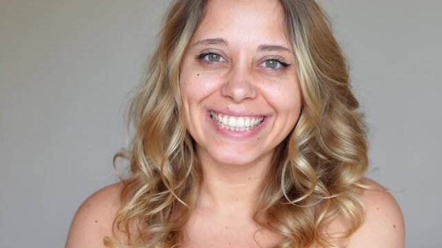 A young attractive cheerful caucasian smiling blonde woman with golden wavy hair with dimples on her cheeks on a grey background. Charming girl with green eyes