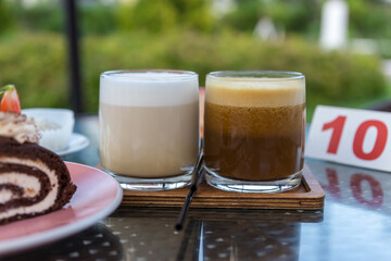 Two glasses of coffee sit on a wooden tray next to a slice of cake