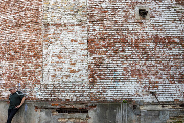 A person stands in front of a brick wall with a window