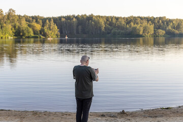Fototapeta premium A man is standing on a beach, taking a picture of the lake