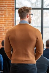 Obraz premium A young professional stands with his back to the camera, engaged in a meeting with others in a modern office environment.