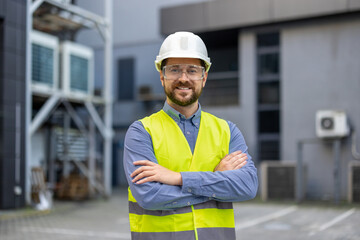 Confident construction worker wearing safety vest and helmet smiling while standing at an...