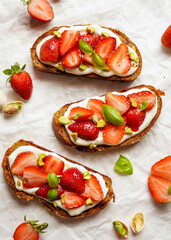 Three slices of open faced sandwich topped with strawberry, greek yogurt, sweet basil leaves, and crushed pistachios, over white background. Flat lay