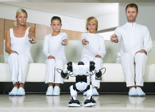 Portrait of Family Sitting on Sofa, Using Remote Controls on Robot