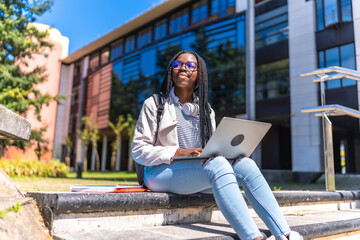 Distracted african woman using laptop sitting outside the university campus
