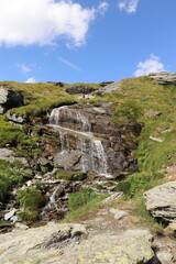 Hidden among the rocks, in a remote corner of the Alps, a medium-sized waterfall creates a delicate melody, inviting contemplation of nature.