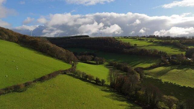 Panning across emerald hills of welsh valley revealing windmills, herd of sheep and cloudy sky