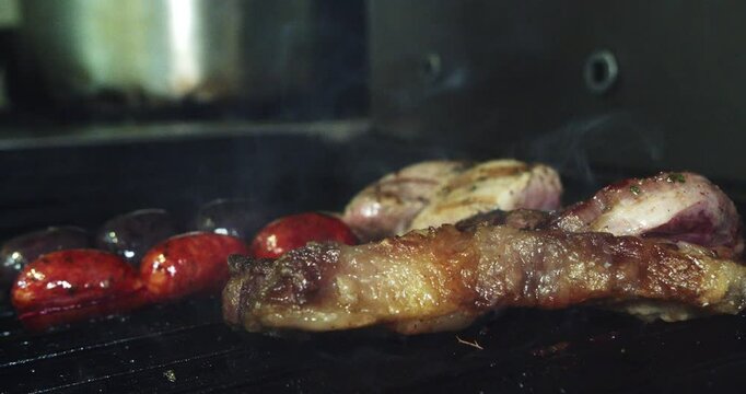 Beautiful slow motion shot of a grilled pork tenderloin on a grill smoking next to a pork loin and chorizo sausages.