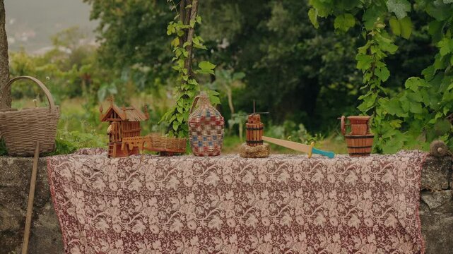Display of traditional handcrafted wooden miniatures and basket on a patterned tablecloth outdoors, in Rural Portugal