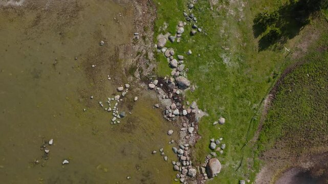 Top down drone shot of coastline in the Baltic sea. Grass and rocks on the shore.