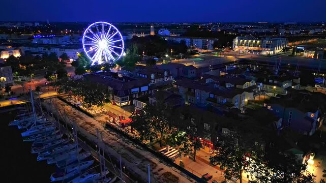 Fly over the old port and Quai Valin with big wheel in background, La Rochelle at night, France. Aerial drone view